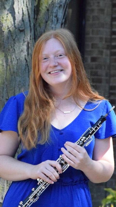 A photo of Joy Anderson, standing and holding her oboe outside.